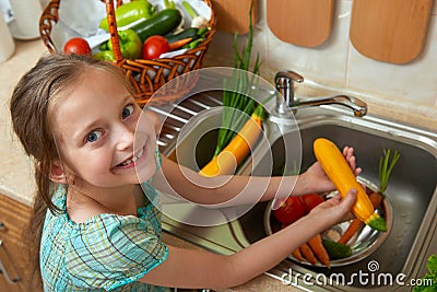 Child girl washing vegetables and fresh fruits in kitchen interior, healthy food concept Stock Photo