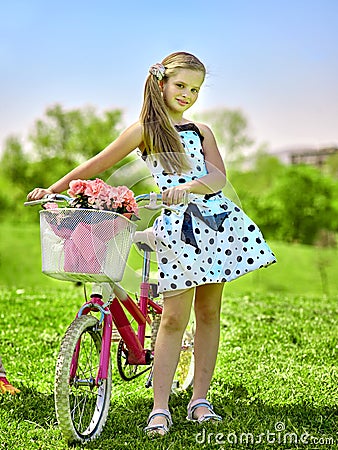 Child girl wearing white polka dots dress rides bicycle into park. Stock Photo