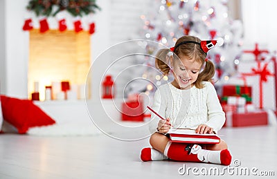 Child girl writing letter santa home near Christmas tree Stock Photo