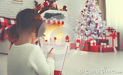 Child girl writing letter santa home near Christmas tree Stock Photo