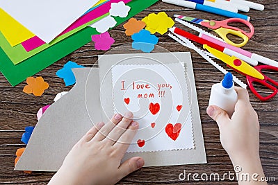 The child glues the details from the paper to the postcard. Greeting card with flowers on Mother`s Day. Stock Photo
