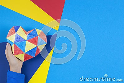 Child hand holding colorful paper heart over multicolored paper background. World autism awareness day concept Stock Photo