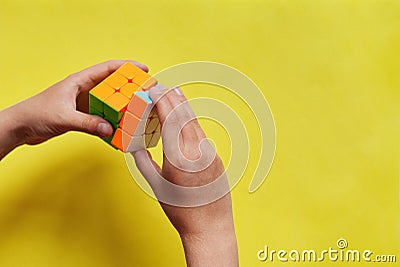 Child hand holding colorful Rubik`s cube on yellow background. Concept of play game and puzzle construction. Closeup, top view Editorial Stock Photo