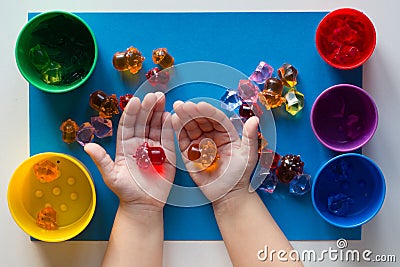 Child hand holding multicolored toys to separating into colorful cups by color on the blue surface Stock Photo