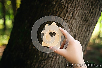 Flat wooden house shape in child hands against a forest background. Stock Photo