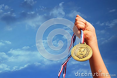 Child hand raised, holding gold medal against sky. education, success, achievement, award and victory concept. Stock Photo