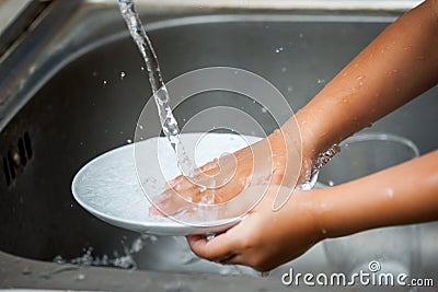 Child hand washing dishes over the sink Stock Photo