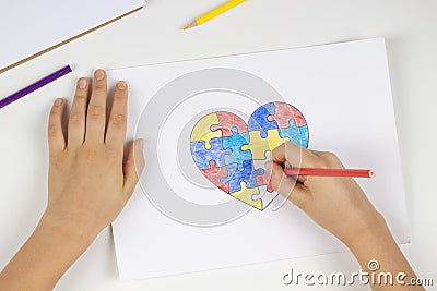 Child hands coloring puzzle heart with colored pencils. Top view. World autism awareness day concept Stock Photo