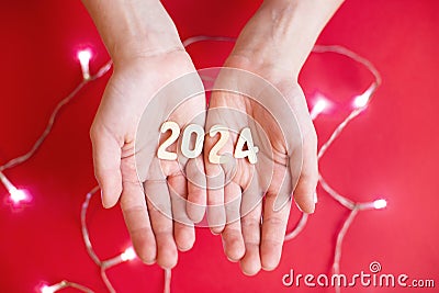 Child hands holding wooden number 2024 on palms on festive red background with copy space Stock Photo