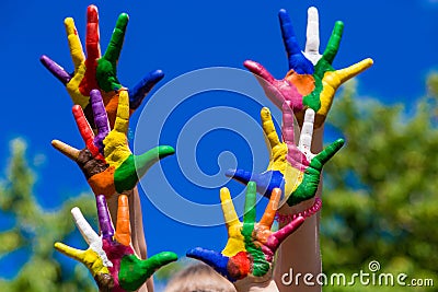 Child hands painted in bright colors isolated on summer nature background Stock Photo