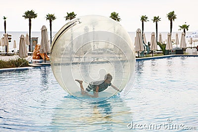 Child have fun inside big plastic balloon on the water of swimming pool on the summer resort. Little boy inside big inflatable Stock Photo