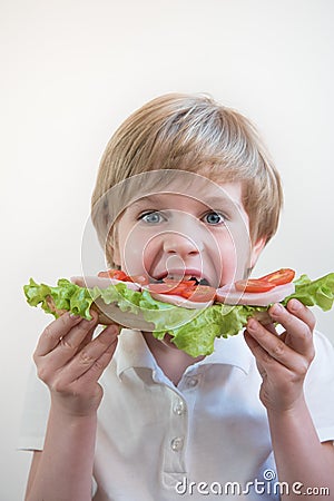 A child with his mouth wide open. Bites into a large ham and vegetable sandwich. School lunch. Portrait, close-up Stock Photo