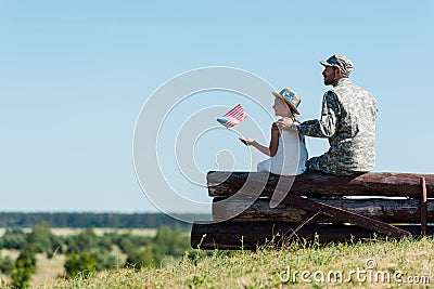 Child holding american flag near father in military uniform while sitting in fence Stock Photo