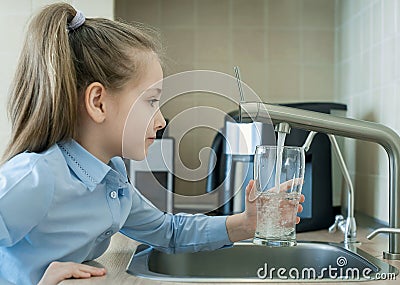 Child is holding a transparent glass. Filling cup beverage. Pouring fresh drink. Consumption of tap water contributes to the Stock Photo