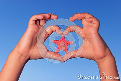 Child holds hands up to sky in the shape of a heart with starfish. Love shape child hands with starfish. Stock Photo