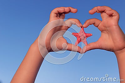 Child holds hands up to sky in the shape of a heart with starfish. Love shape child hands with starfish. Stock Photo