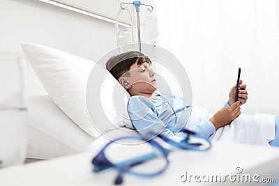 Child in hospital bed using smartphone surfs the internet wearing earphones Stock Photo