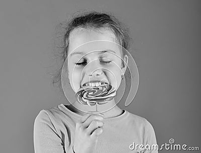 Child with hungry face poses with candy on green background. Treatment and sweets concept. Lady holds round shaped Stock Photo