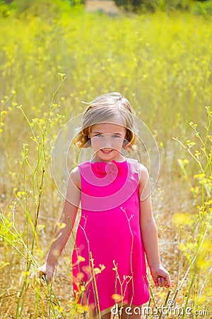 Child kid girl in spring yellow flowers field and pink dress Stock Photo