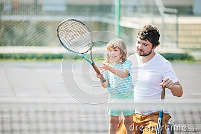 Child learning to play tennis with her father on outdoor court. Little girl with tennis racket Stock Photo