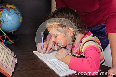A child learns to write in a notebook. Mom helps her daughter do her homework. The concept of home education in quarantine. A Stock Photo