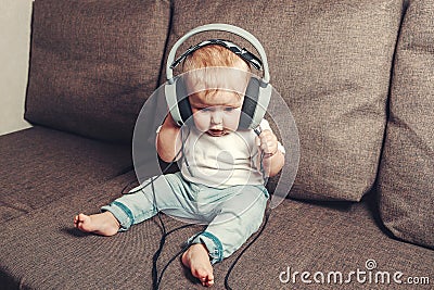 Child learns the world. A little happy child is sitting on bed in big headphones and listening to music Stock Photo