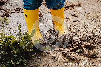 Child legs in yellow muddy rubber boots on wet mud. Baby playing with dirt at rainy weather. Stock Photo