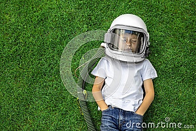 child lies on the grass wearing an astronaut`s helmet and dreams of great achievements Stock Photo