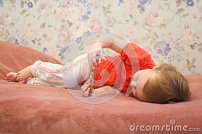 Child little baby girl lying on bed with smartphone in hands. Stock Photo