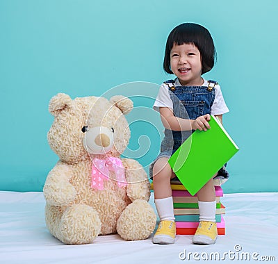 Child little girl or a little cute girl reading a book in the green background and sitting on the books with a toy Stock Photo