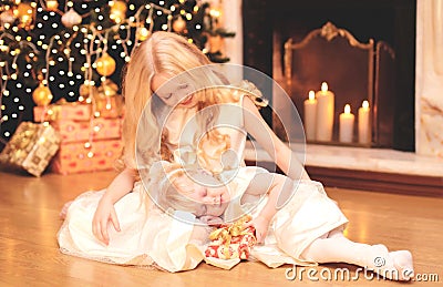 Child little girl gives a gift box to sister over christmas tree and fireplace home Stock Photo