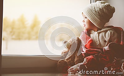 Child little girl with teddy bear at window and looking at wint Stock Photo