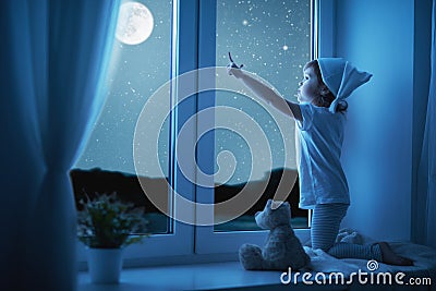 Child little girl at window dreaming and admiring starry sky at Stock Photo