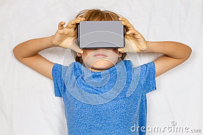 Child liying in bed with 3D Virtual Reality, VR cardboard glasses Stock Photo