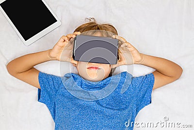 Child liying on bed with 3D Virtual Reality, VR cardboard glasses Stock Photo