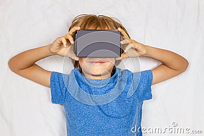 Child liying in white bed with 3D Virtual Reality, VR cardboard glasses Stock Photo