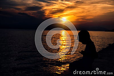 The child looks into the smartphone on the background of a beautiful sunset Stock Photo