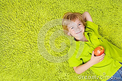 Child lying on the green carpet, holding apple Stock Photo