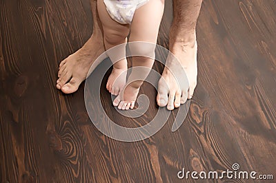 The child makes the first step. Large male legs with small baby legs. Dad helps the child take the first steps Stock Photo