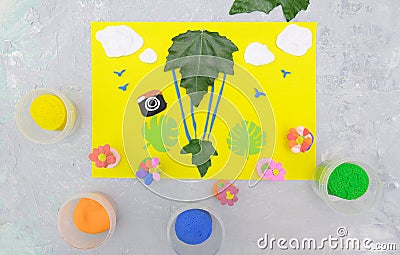 Child making card from paper, plasticine and natural leaves. Air balloon, clouds, birds, flowers... Inspiration for children. Stock Photo