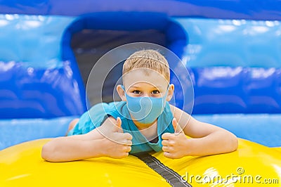 Child with mask on colorful playground trampoline. Kids jump in inflatable bounce castle on kindergarten birthday party. Activity Stock Photo