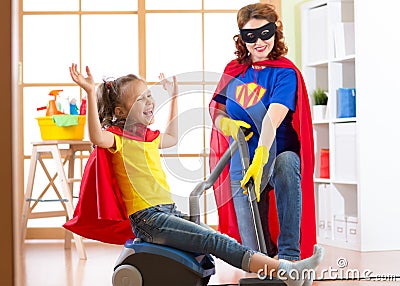 Child and mommy dressed as superheroes using vacuum cleaner in room. Family - woman and kid daughter have a fun while Stock Photo