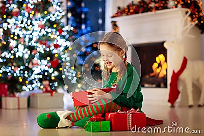 Child opening present at Christmas tree at home. Kid in elf costume with Xmas gifts and toys. Little girl with gift box and candy Stock Photo