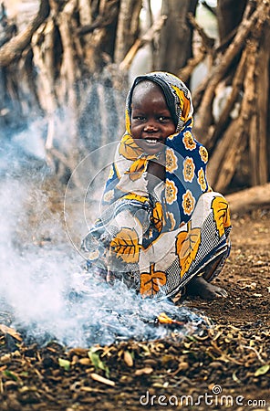 TOPOSA TRIBE, SOUTH SUDAN - MARCH 12, 2020: Child in ornamental cloth smiling and looking at camera while sitting on haunches near Editorial Stock Photo