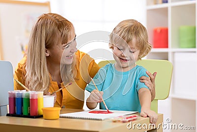 Child painting in preschool. Teacher help by little boy. Stock Photo