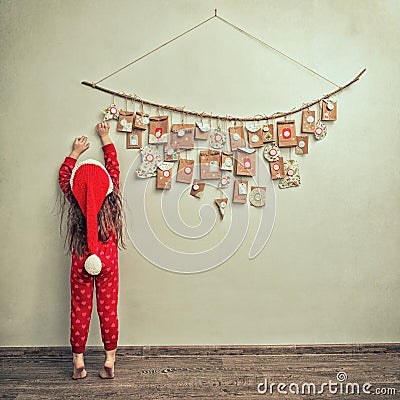 Child in pajamas and Christmas cap stretches for advent calendar with small gifts. kid counts days until new year Stock Photo