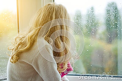 A child in pajamas smiles in an autumn window with rain drops. Stock Photo