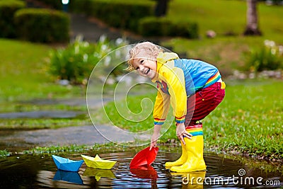 Child with paper boat in puddle. Kids by rain Stock Photo