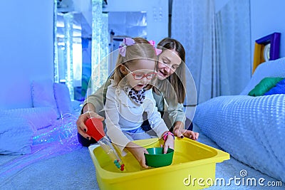 Child with physical disability in sensory stimulating room, snoezelen. Child living with cerebral palsy interacting with therapist Stock Photo