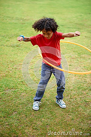 Child, playing and hula hoop on field on holiday, green grass and sunshine with energy in city. Young boy, mexican and Stock Photo